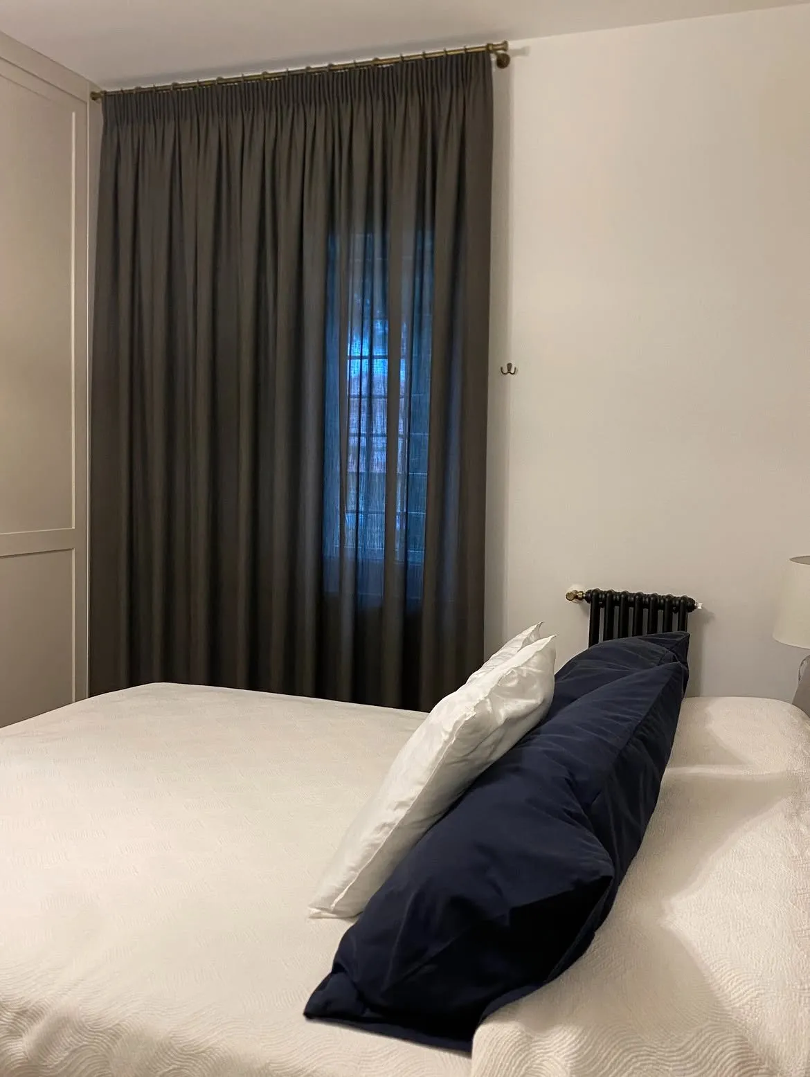 Tende antracite accanto al letto con cuscini blu